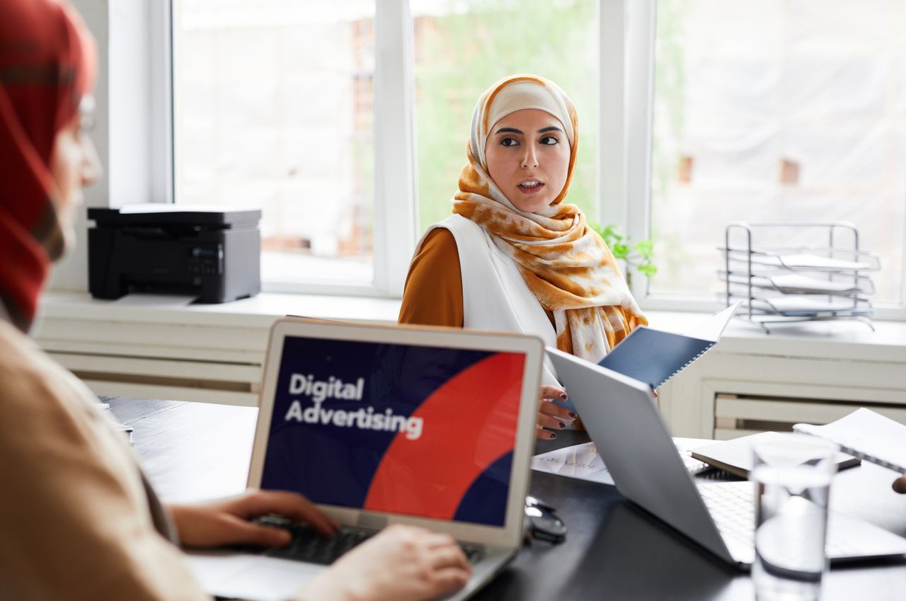 gallery-2 Two women in hijabs discuss digital advertising in an office setting.